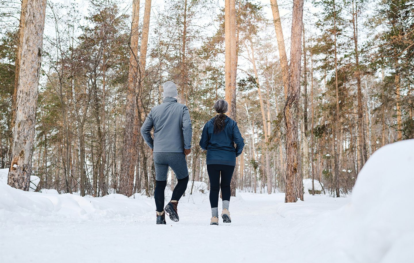 two people hiking in the woods with snow covering the ground